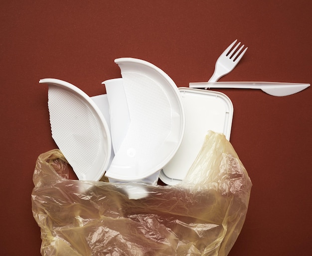 used plastic dishes pieces of plastic and a white plastic bag on a brown background top view flat