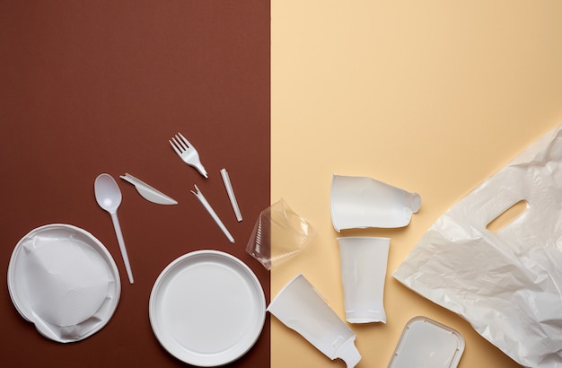 Used plastic dishes, pieces of plastic and a white plastic bag on a brown background, top view