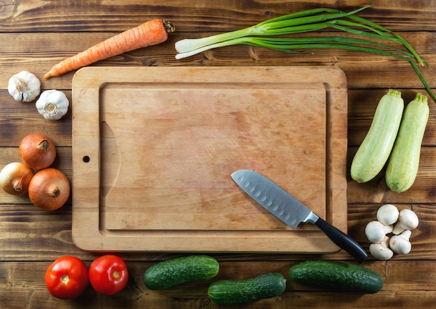 Photo used rustic wooden chopping board, knife and raw vegetables on dark table