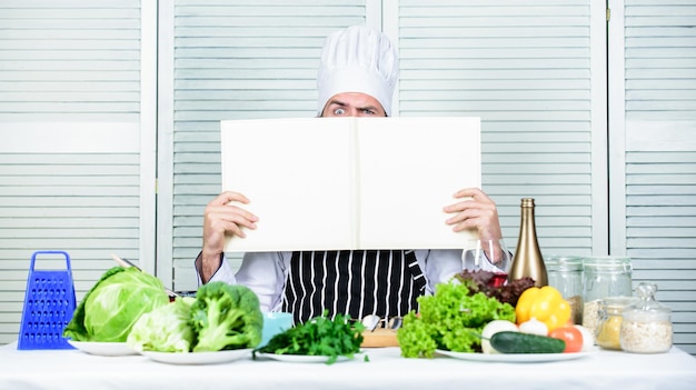 料理に役立つ本。料理のキャリアを開始します。ステップバイステップの究極の料理ガイド。本のレシピはスペースをコピーします。帽子とエプロンの男のシェフは本を読みます。料理レシピ本のコンセプト。料理のスキルを向上させます。