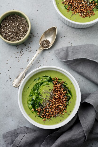 Useful smoothies from spinach with buckwheat flakes in ceramic bowls on gray concrete table background