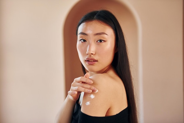 Photo uses beauty cream young serious asian woman standing indoors