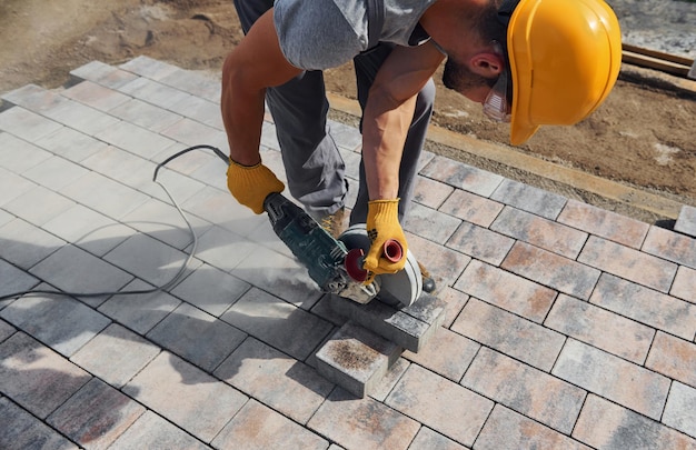 Photo uses circular saw male worker in yellow colored uniform have job with pavement