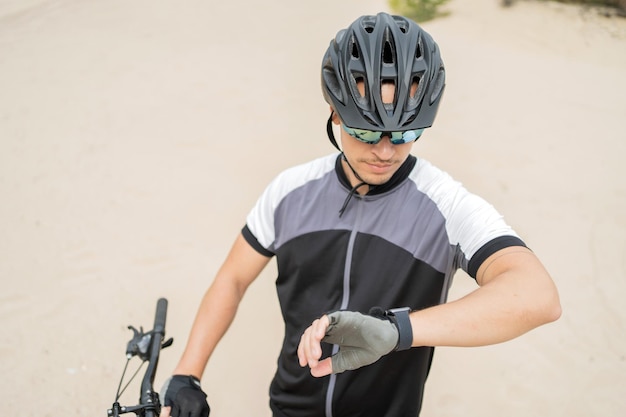 Utilizza un orologio fitness un uomo su una mountain bike in un casco e attrezzature ecoturistiche