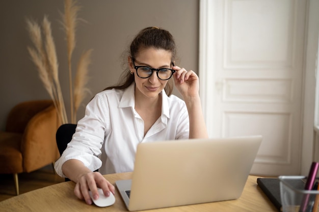 Uses a laptop computer a woman with glasses looks at the camera in a white shirt