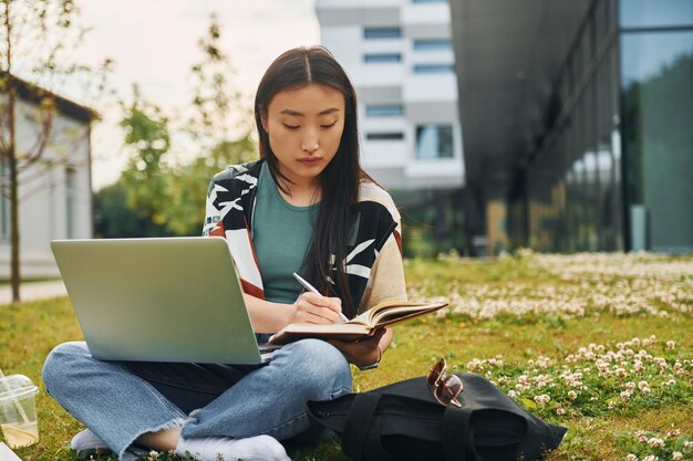 Uses laptop Young asian woman is outdoors at daytime