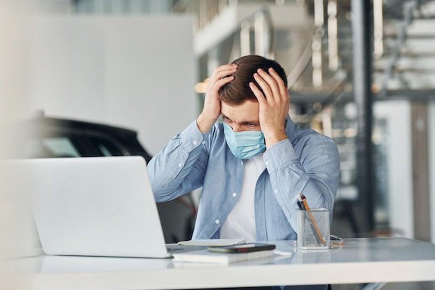 Uses laptop Young man in white shirt and blue jacket works indoors