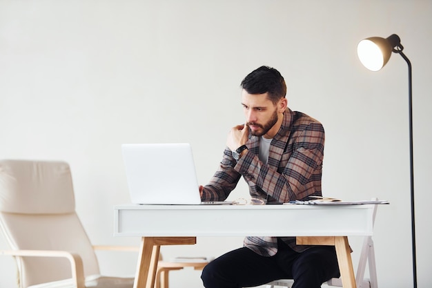 Uses laptop Young stylish businessman in suit indoors Conception of success