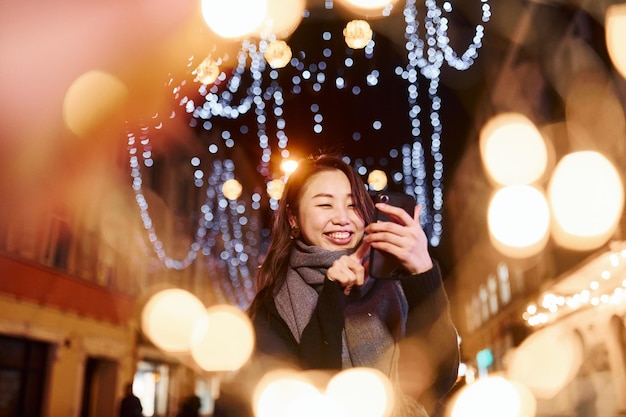 전화 사용 도시에서 야외에서 귀엽고 행복한 아시아 젊은 여성이 새해를 축하합니다