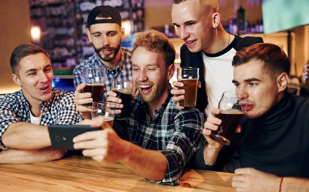 Usa il telefono gruppo di persone insieme al chiuso nel pub si divertono durante il fine settimana