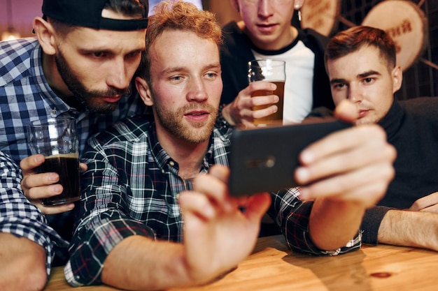 Uses phone group of people together indoors in the pub have fun\
at weekend time