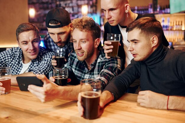 Uses phone Group of people together indoors in the pub have fun at weekend time