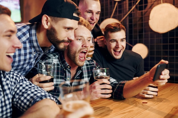 Uses phone group of people together indoors in the pub have fun\
at weekend time