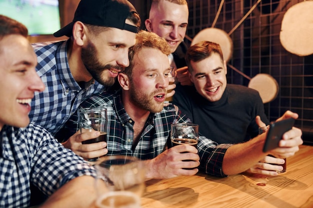 Uses phone group of people together indoors in the pub have fun\
at weekend time