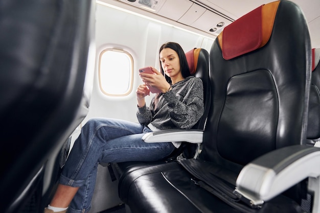 Photo uses phone young woman in casual clothes sits on the passenger seat in the plane