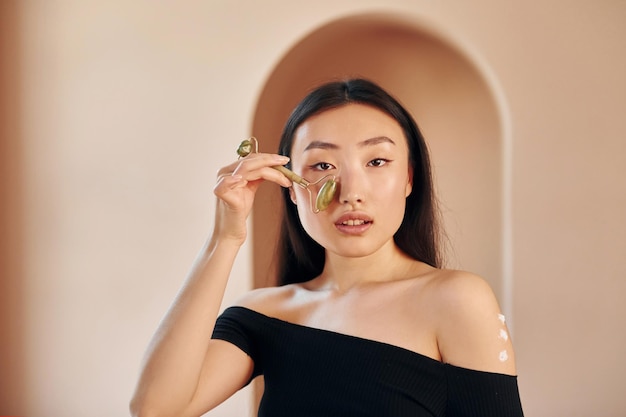 피부 청소 도구를 사용하여 실내에 서 있는 젊은 진지한 아시아 여성