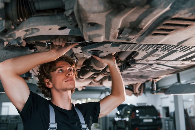 Uses wrench to fix car Adult man in grey colored uniform works in the automobile salon