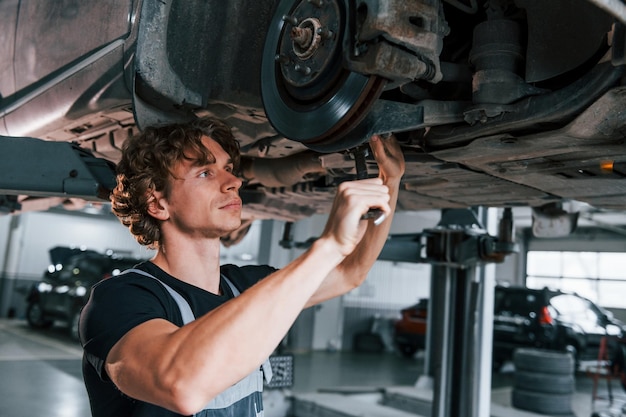 Uses wrench to fix car Adult man in grey colored uniform works in the automobile salon