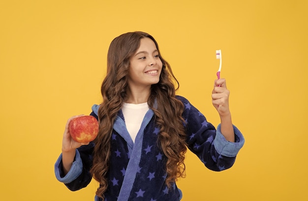 Using best toothpaste childrens stomatology teen girl with toothbrush and apple happy kid brush her teeth child in pajama do morning routine dental everyday care healthy beautiful smile