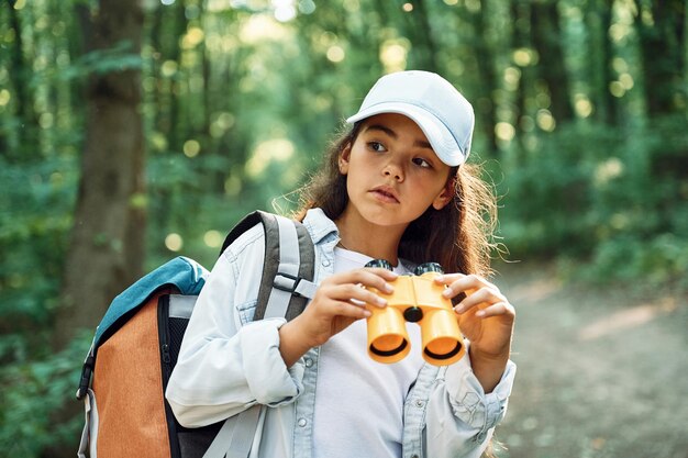 Using the binoculars Girl is in the forest at summer day time discovering new places