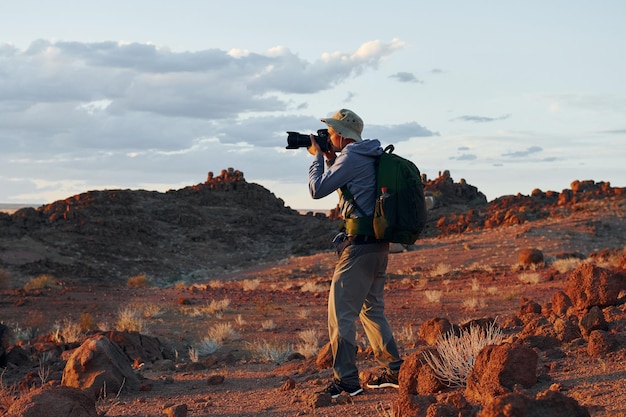 카메라 사용 캐주얼 옷을 입은 남성 관광객은 아프리카 나미비아의 사막에 있습니다