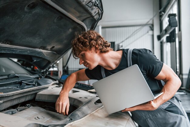 Using computer Adult man in grey colored uniform works in the automobile salon