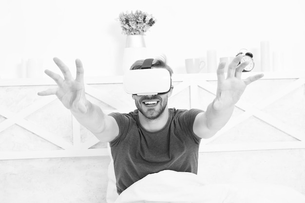 Photo using computer technology to create a simulated environment happy guy wearing vr headset for computer gaming handsome man playing virtual computer games in bed gaming computer