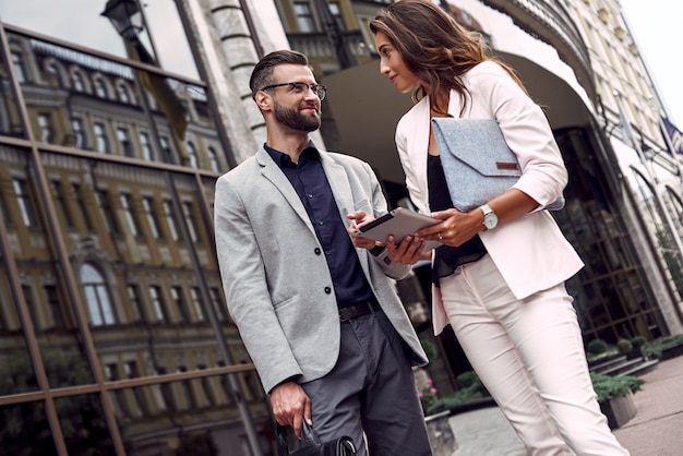 Using gadget two young business people standing outside on the city street using digital tablet