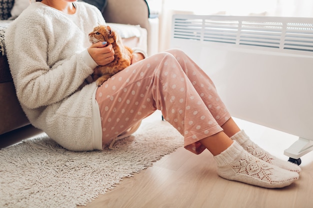 Фото Использование обогревателя в домашних условиях зимой. женщина потепление тела с кошкой. отопительный сезон.