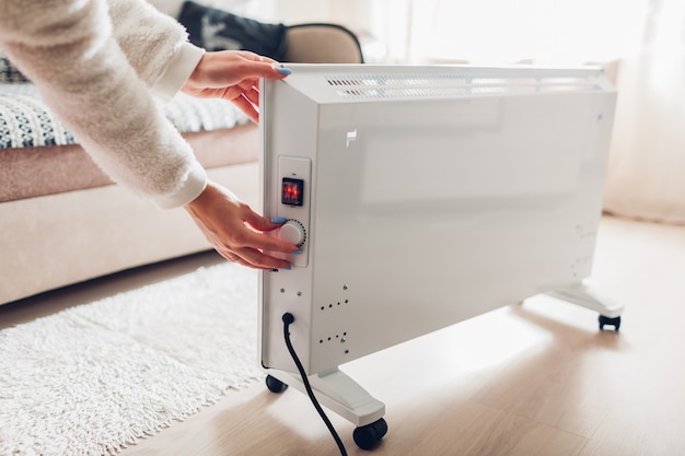using heater at home in winter. woman regulating temperature on heater. heating season.