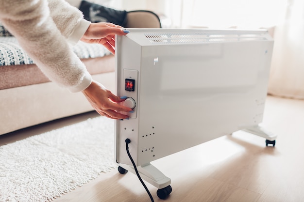 Using heater at home in winter. Woman regulating temperature on heater. Heating season.