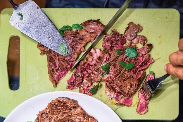 Foto usando il coltello per affettare la bistecca di manzo su una tavola tritata e una forchetta per pugnalare la carne