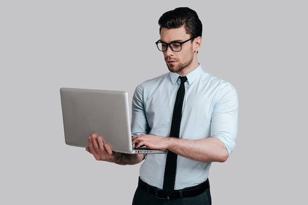 using laptop.  Businessman posing against the white wall