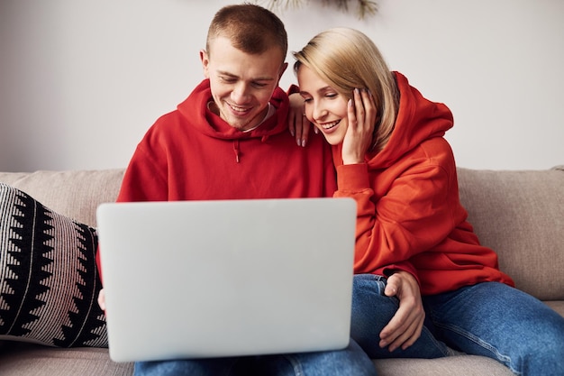 Photo using laptop that is on the legs young lovely couple together at home spending weekend and holidays together