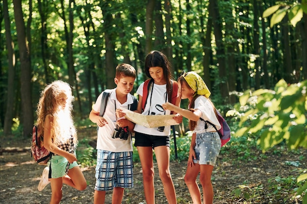 Использование карты, чтобы найти дорогу Дети гуляют по лесу с туристическим снаряжением