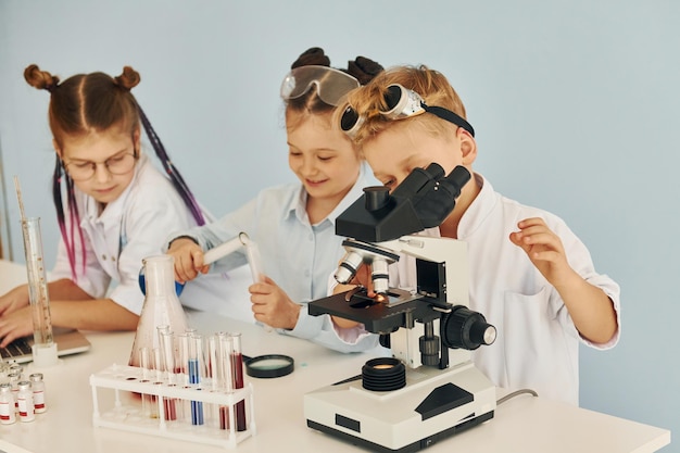 Using microscope Children in white coats plays a scientists in lab by using equipment