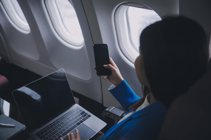 Photo 携帯電話とラップトップを使って 考え深いアジア人 女性が飛行機の窓から 休暇旅行の期待と興奮を 完璧に捉えています