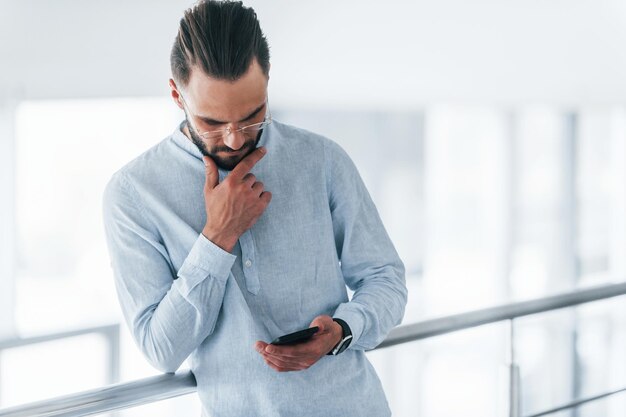 電話を使用して日中のオフィスの屋内でフォーマルな服を着た若いハンサムな男