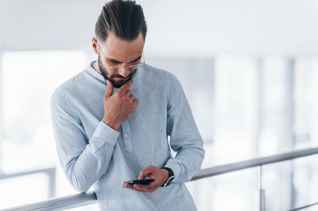 Using phone Young handsome man in formal clothes indoors in the office at daytime