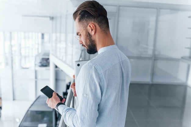 電話を使用して日中のオフィスの屋内でフォーマルな服を着た若いハンサムな男