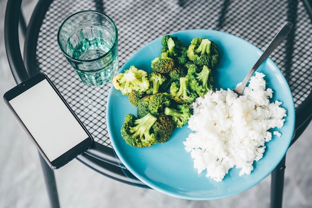 Foto usare lo smartphone mentre si mangia broccoli e riso a casa