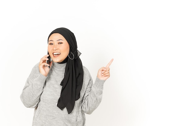 Using smartphone and pointing aside of Beautiful Asian Woman Wearing Hijab Isolated On White