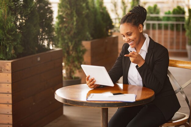 Using tablet, pointing. African-american businesswoman in office attire smiling, looks confident happy, busy. Finance, business, equality and human rights concept. Beautiful young model, successful.