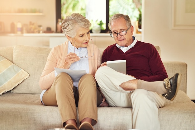 Using their tablet to do the grunt work Shot of an elderly couple working out a budget while sitting on the living room sofa