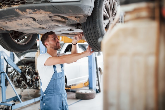 Using a wrench. Employee in the blue colored uniform works in the automobile salon