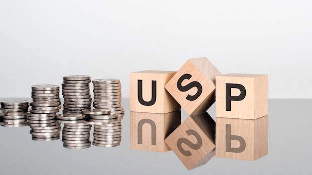 Usp Unique Selling Proposition text is made up of letters on wooden cubes lying on a mirror surface gray background stacks with coins inscription is reflected from the surface selective focus