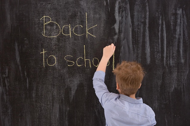 Сute Lefthanded kid boy writing Back to school with chalk on the blackboard in classroom