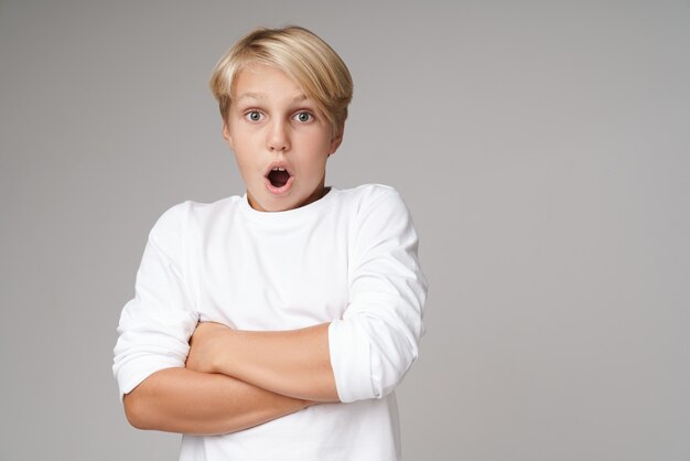 ute opgewonden kleine blonde jongen met een sweatshirt dat geïsoleerd over een grijze muur staat