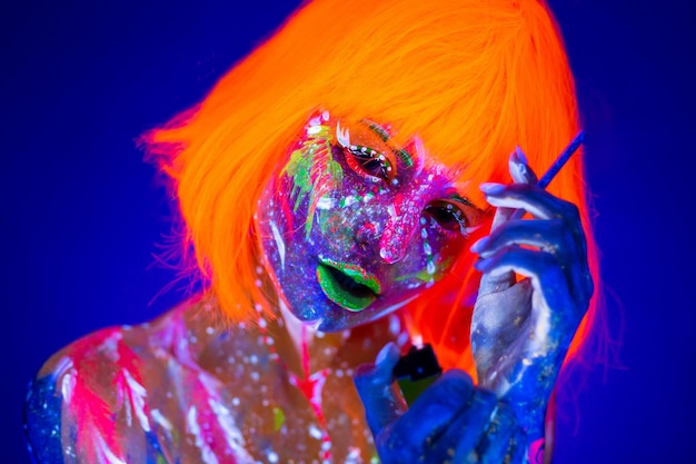 UV portrait of a female model with artistic colorful makeup and an orange wig with a cigarette