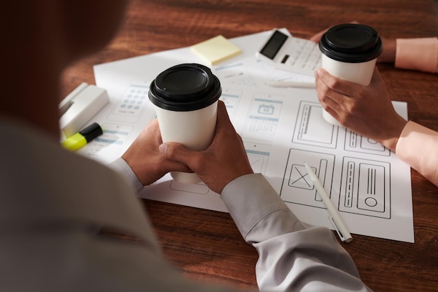 회의에서 모형 및 프로젝트 문서를 논의할 때 테이크아웃 커피를 마시는 Ux 디자이너